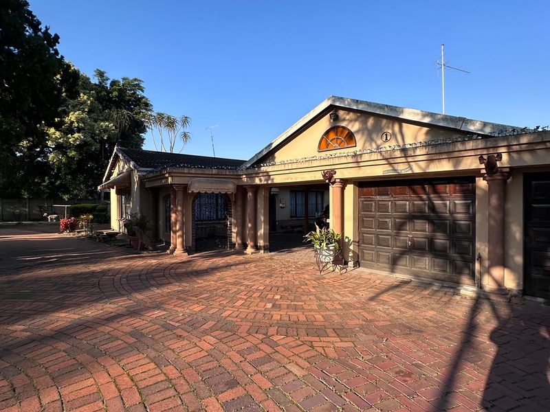 Front elevation of a single-story house featuring a large brick-paved driveway, double garage, and decorative architectural columns under a clear blue sky.