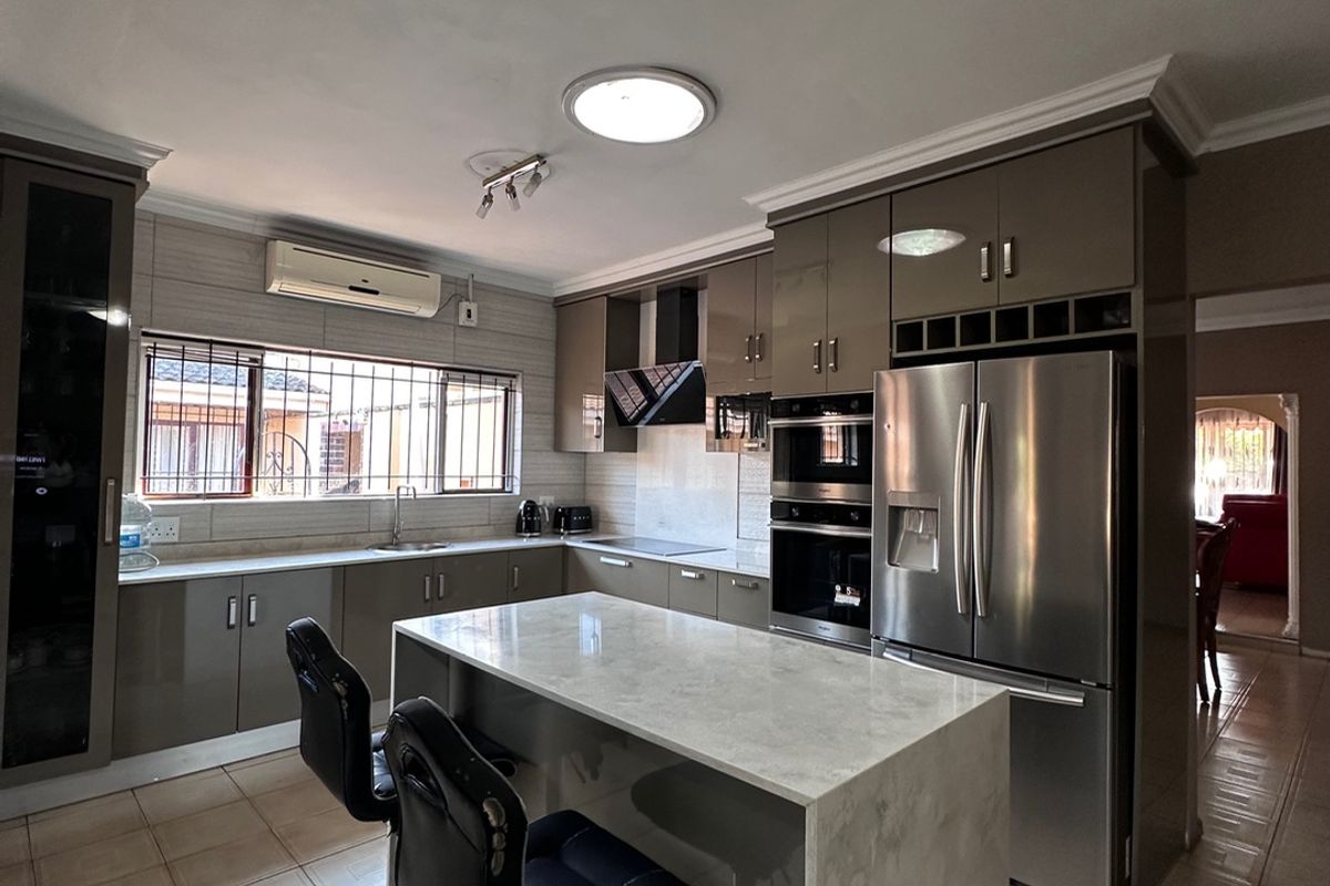 Modern kitchen featuring high-gloss cabinetry, stone-topped island, built-in appliances, and tiled flooring, offering a functional and contemporary cooking space.