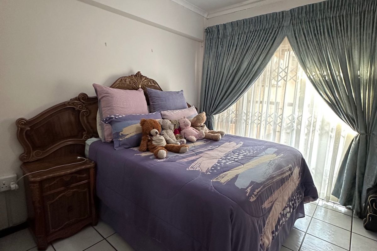 A bedroom featuring tiled flooring, a ceiling fan, and large windows with security gates, offering a functional space ready for cosmetic updates.