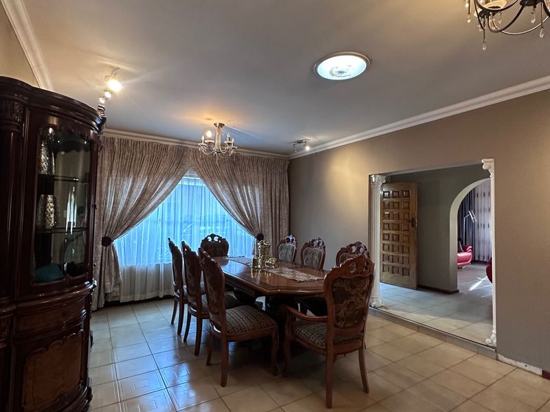 Spacious dining room featuring ceramic floor tiles, decorative archway, and classic chandelier lighting, offering a traditional layout with direct access to adjacent living areas.