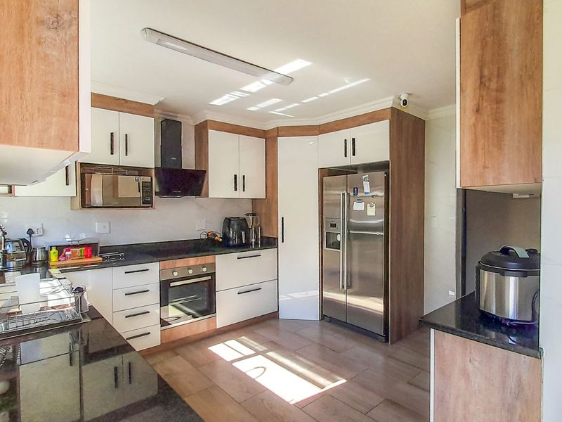 Modern kitchen featuring wood-tone and white cabinetry, granite countertops, built-in oven, extractor fan, and integrated microwave with tiled flooring.