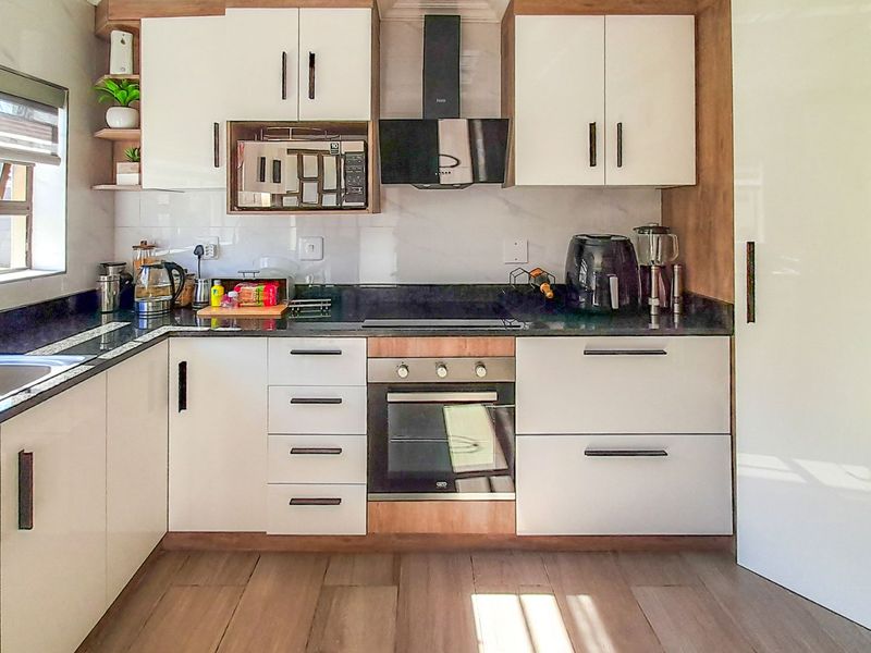 Modern kitchen featuring sleek white cabinetry, granite countertops, integrated appliances including an oven and extractor fan, and durable laminate flooring.