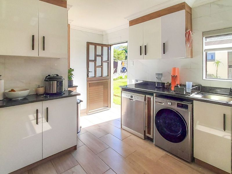 Modern kitchen featuring white cabinetry, dark stone countertops, tiled flooring, and integrated appliances with direct access to the rear garden.