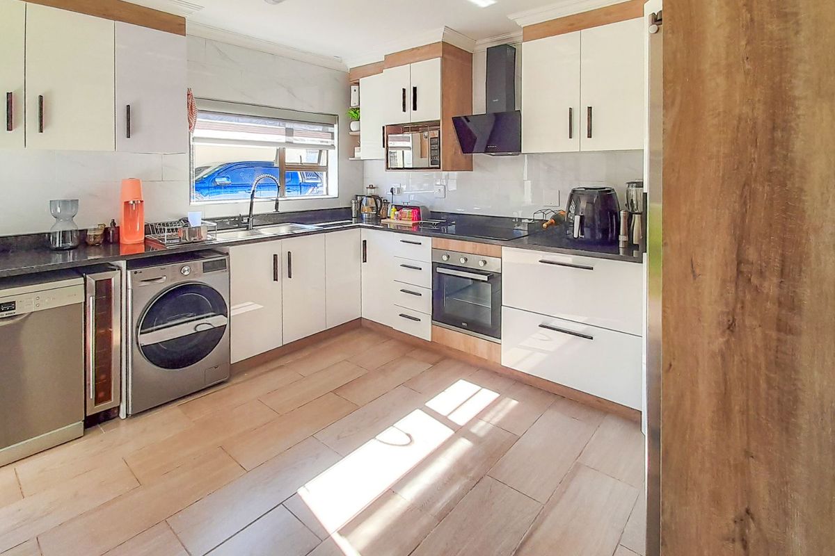 Modern kitchen featuring white cabinetry, stone countertops, integrated oven, extractor fan, and tiled flooring with ample natural light.