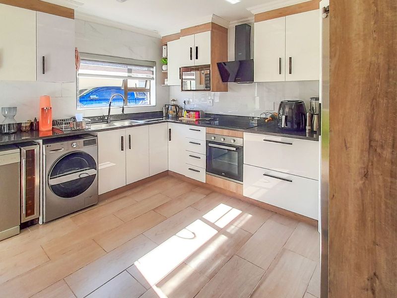 Modern kitchen featuring white cabinetry, stone countertops, integrated oven, extractor fan, and tiled flooring with ample natural light.