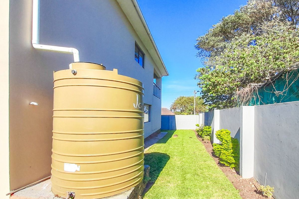 Rear exterior view of the property featuring a water storage tank, lawn area, and perimeter boundary wall.