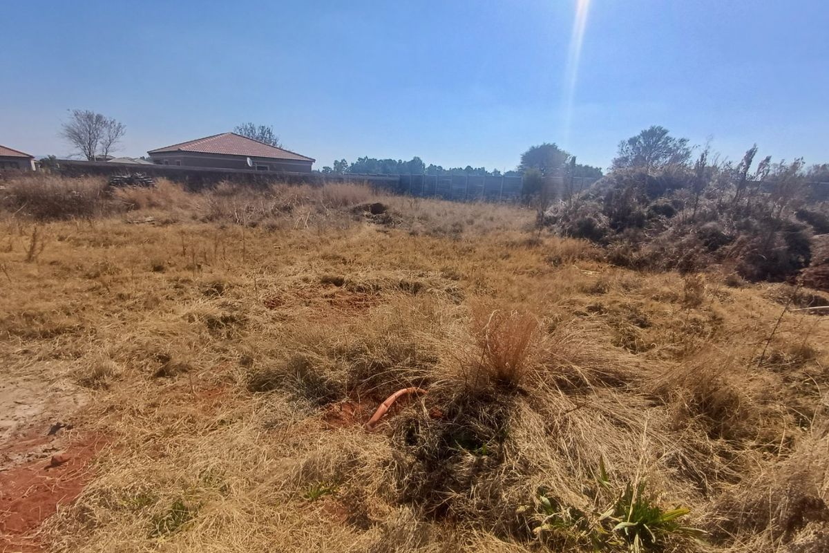 A vacant residential plot featuring dry grass, perimeter walling, and some debris, offering a blank canvas for future development.