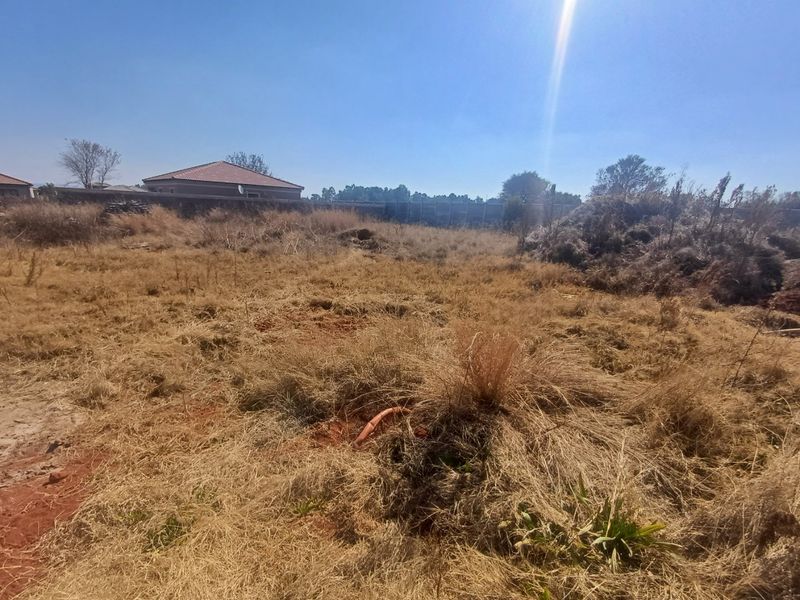 A vacant residential plot featuring dry grass, perimeter walling, and some debris, offering a blank canvas for future development.