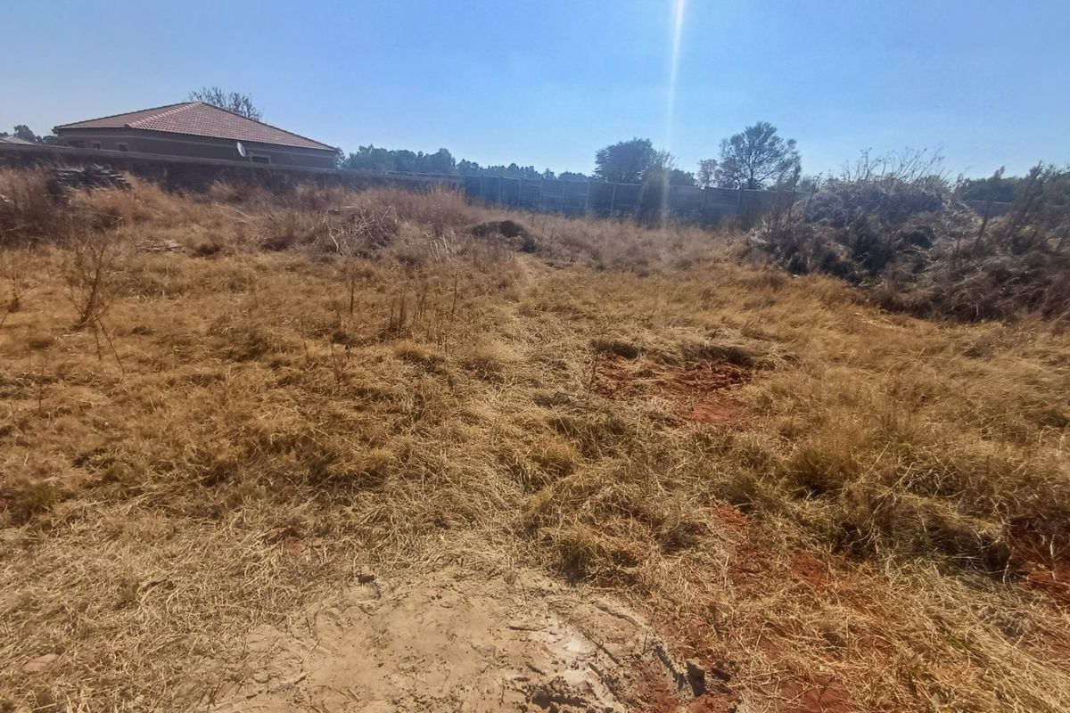 A vacant residential plot featuring dry grass, uneven terrain, and perimeter boundary walls, offering a blank canvas for future development.