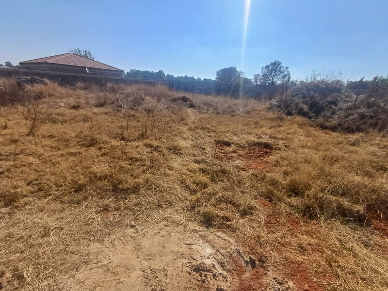 A vacant residential plot featuring dry grass, uneven terrain, and perimeter boundary walls, offering a blank canvas for future development.