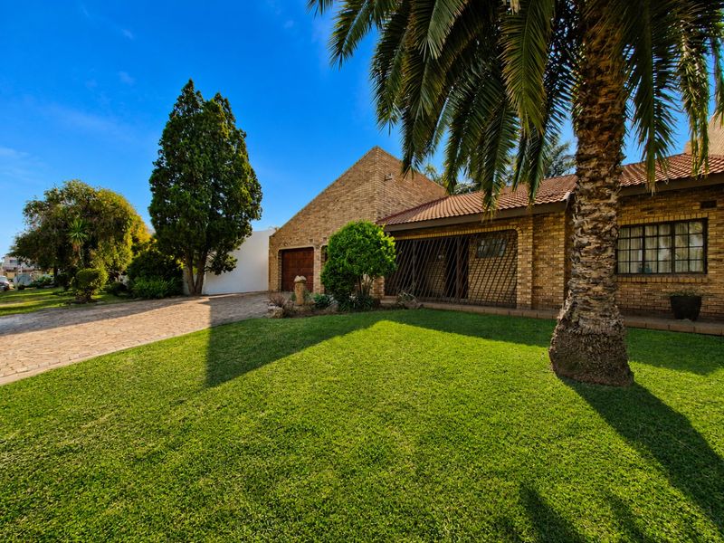 Front view of a brick-faced house featuring a paved driveway, manicured lawn, and secure gated entrance.
