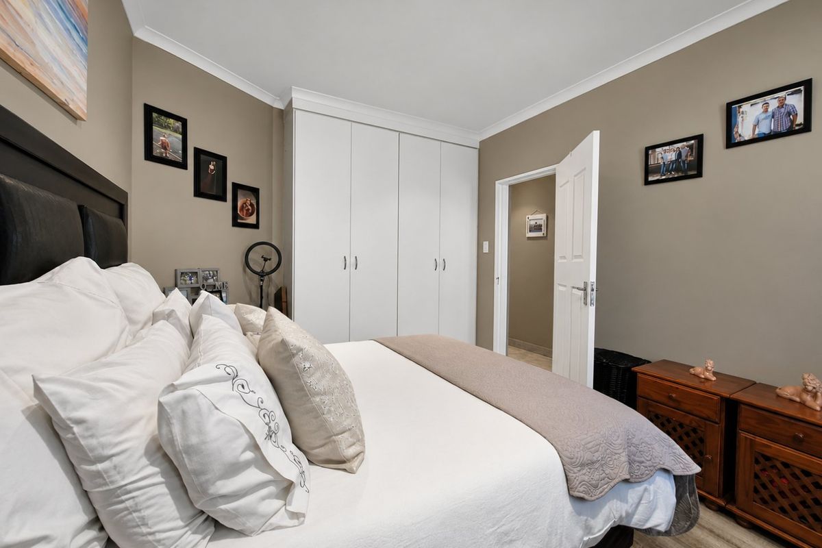 A well-maintained bedroom featuring neutral wall tones, built-in cupboards, and durable laminate flooring, offering a comfortable and functional living space.