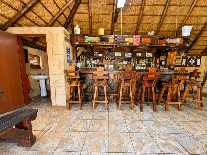 Rustic entertainment bar area featuring a thatched roof, stone wall accents, built-in bar counter, and an adjoining small washroom with a pedestal basin.