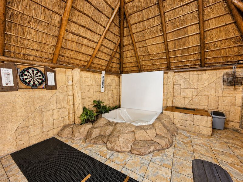 Covered outdoor entertainment area featuring a thatched roof, stone-clad walls, and a built-in spa bath set into a rock-style surround.
