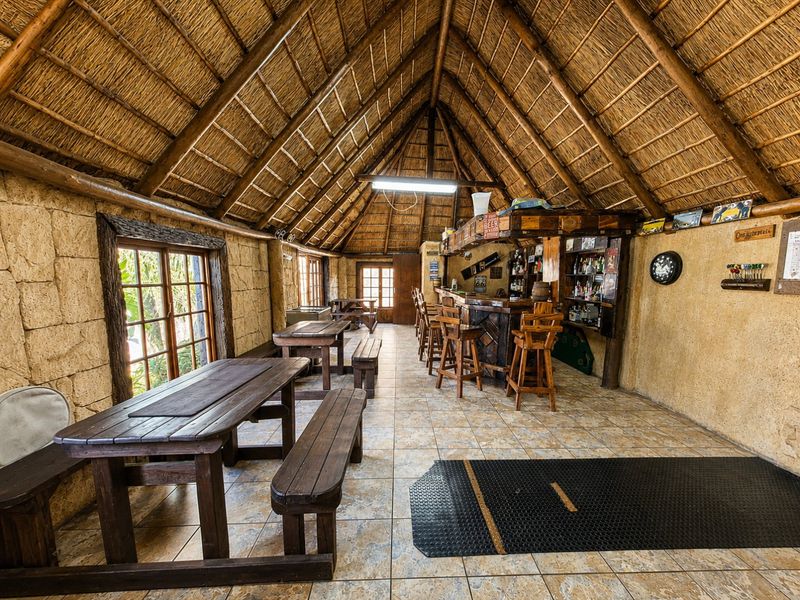 A rustic entertainment bar area featuring a high thatched roof with exposed timber rafters, stone-clad walls, and tiled flooring.