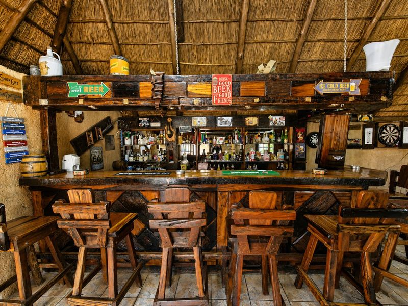 A rustic-style indoor bar area featuring a solid timber counter, custom shelving, and a traditional thatched roof finish.