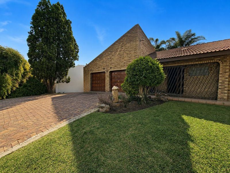 Front exterior view of a brick house featuring a paved driveway, double garage, and landscaped front garden area.