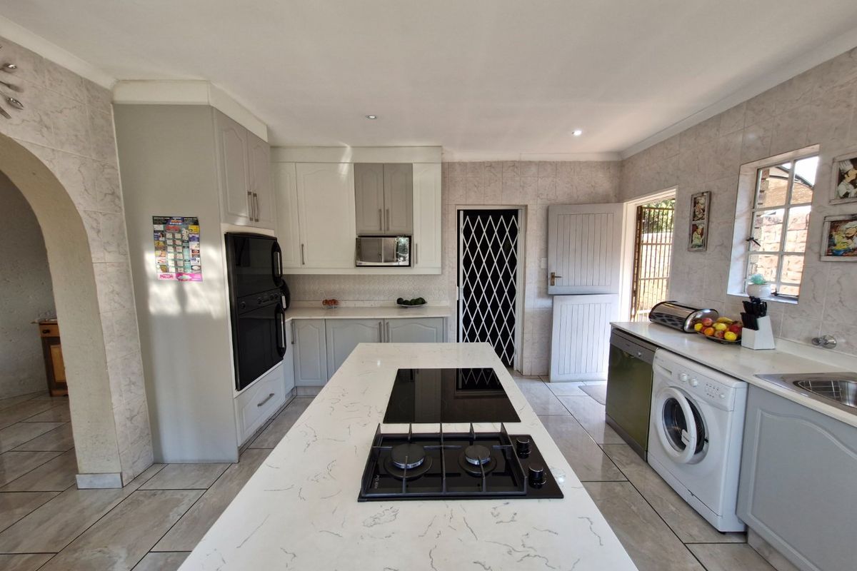 Modern kitchen featuring a central island with a gas hob, stone countertops, built-in oven, and ample cabinetry, leading to an exterior stable door.