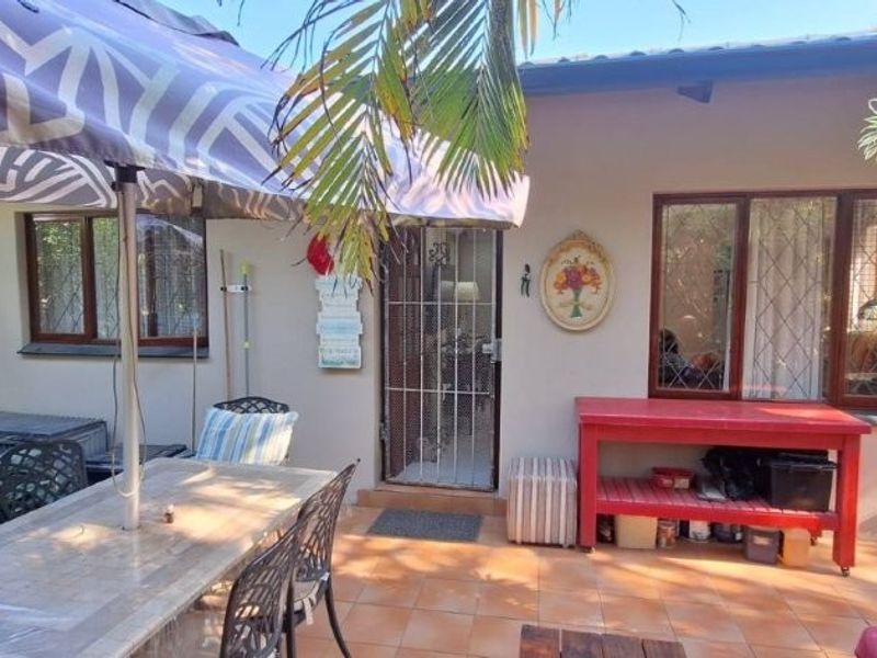 A paved outdoor patio area featuring tiled flooring, security gate access, and window security bars, providing a functional space for outdoor living.