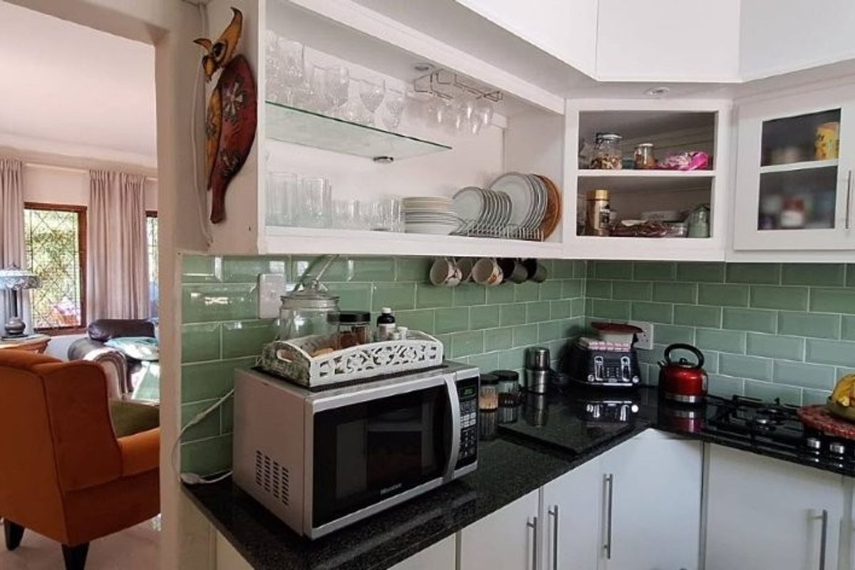 A functional kitchen featuring green subway tile backsplash, dark granite countertops, a gas hob, and white cabinetry with glass-front display sections.