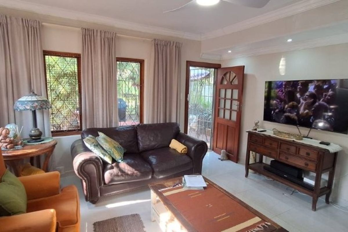 A comfortable living room featuring tiled flooring, recessed lighting, a ceiling fan, and direct access to the outdoor area through a wooden door.