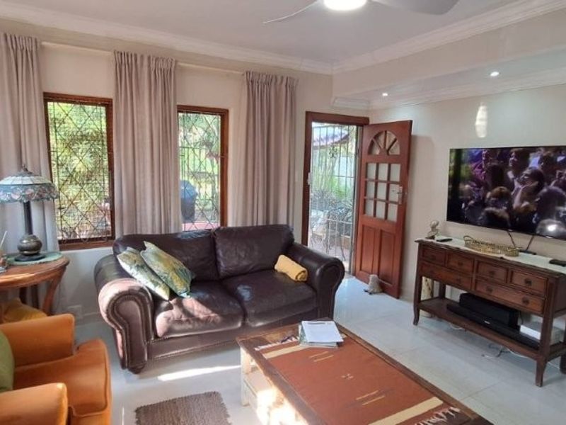 A comfortable living room featuring tiled flooring, recessed lighting, a ceiling fan, and direct access to the outdoor area through a wooden door.