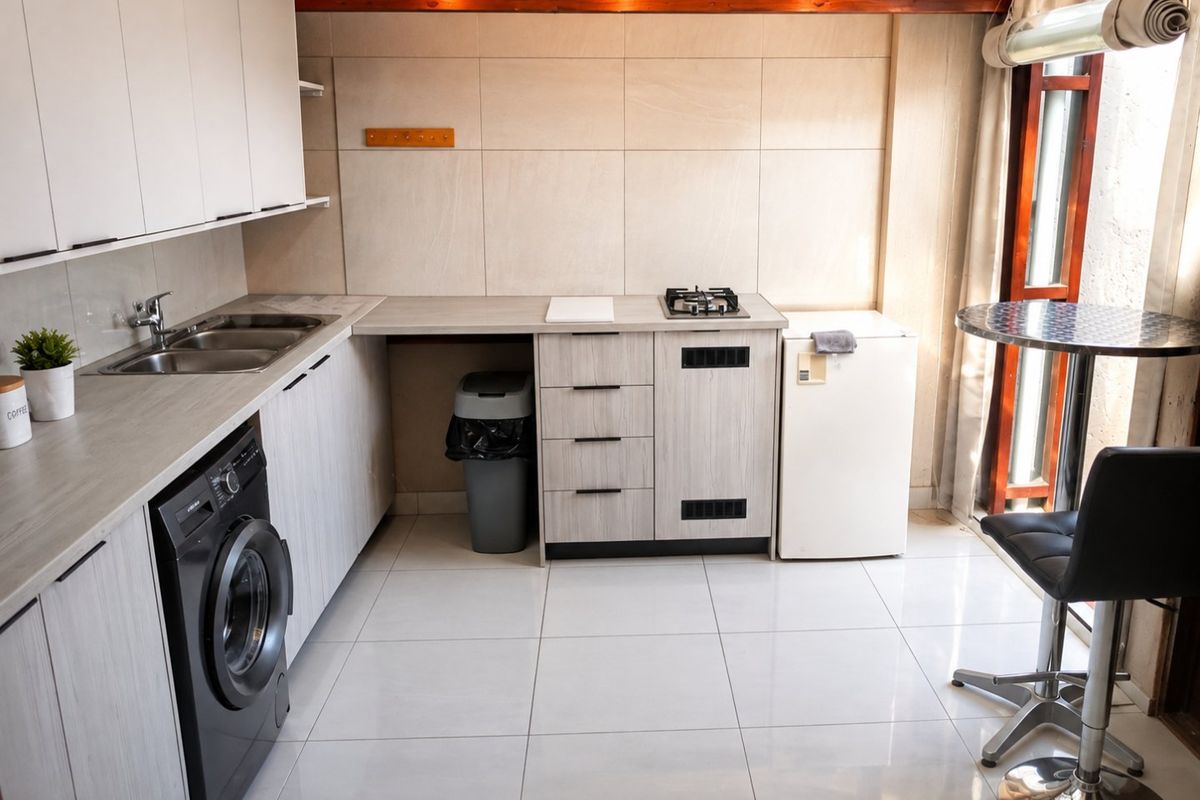 Compact modern kitchen featuring light wood-grain cabinetry, stainless steel sink, gas hob, tiled flooring, and an exposed timber beam ceiling detail.