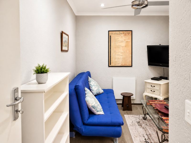 A compact living room featuring a ceiling fan, recessed lighting, and a wall-mounted heater, providing a functional and cozy space.