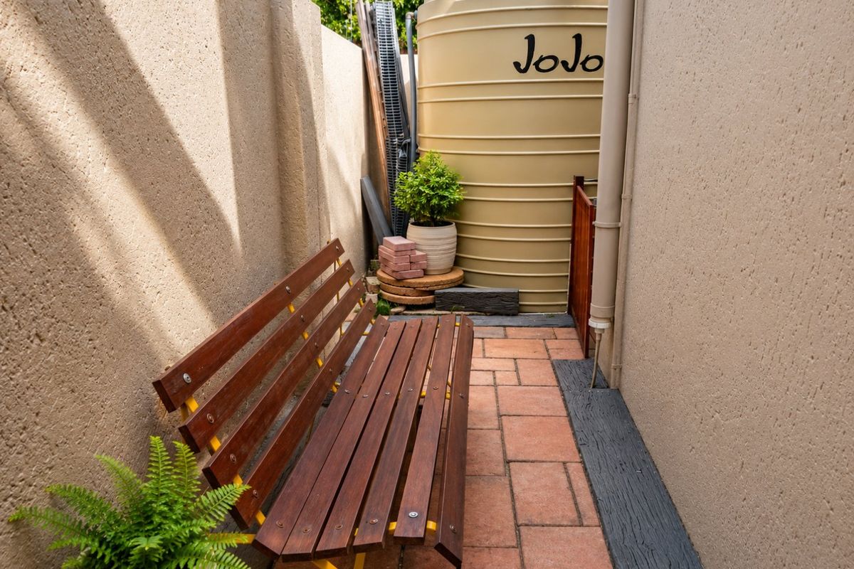 A narrow side passage featuring paved flooring, a boundary wall, and a fixed water storage tank.