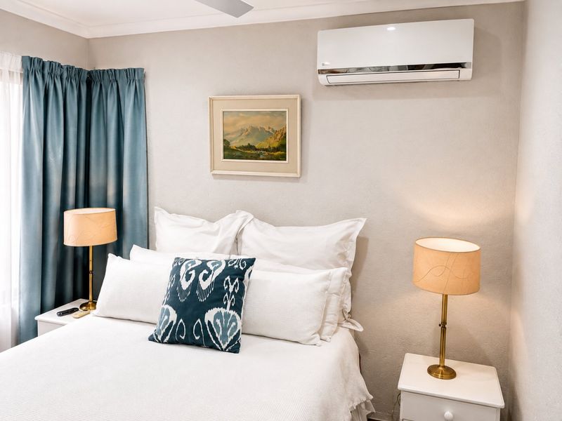 A well-maintained bedroom featuring a wall-mounted split-system air conditioner and a ceiling fan, providing comfortable climate control.