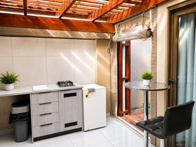 Covered patio area featuring a wooden pergola, built-in cabinetry with a gas hob, and tiled flooring, providing a functional outdoor cooking and dining space.
