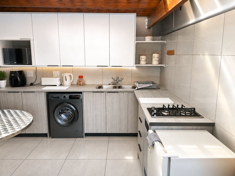 Modern kitchen featuring light wood-grain cabinetry, stainless steel double sink, gas hob, extractor fan, built-in microwave, and exposed timber ceiling beams.