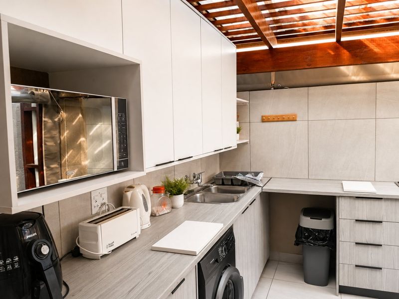 Modern kitchen featuring light wood-grain cabinetry, laminate countertops, a stainless steel double sink, and a unique timber pergola ceiling detail.