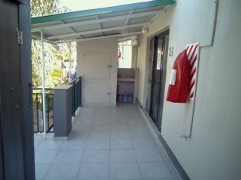 A covered balcony area featuring tiled flooring, a metal balustrade, and a built-in utility alcove, providing a functional outdoor space for the apartment.