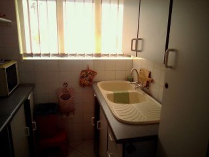 A compact kitchen area featuring a double bowl sink, tiled splashback, and built-in cabinetry with laminate countertops.