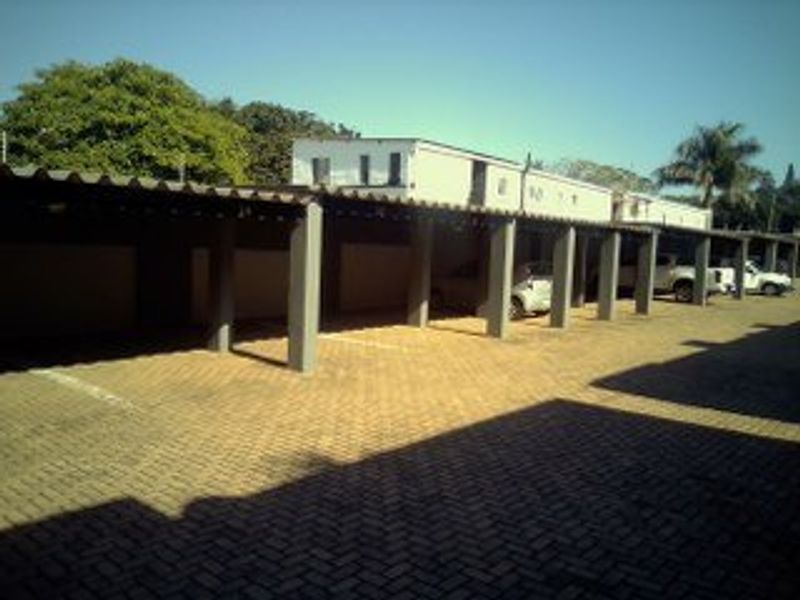 A row of covered parking bays featuring concrete support pillars and a paved driveway area within an apartment complex.