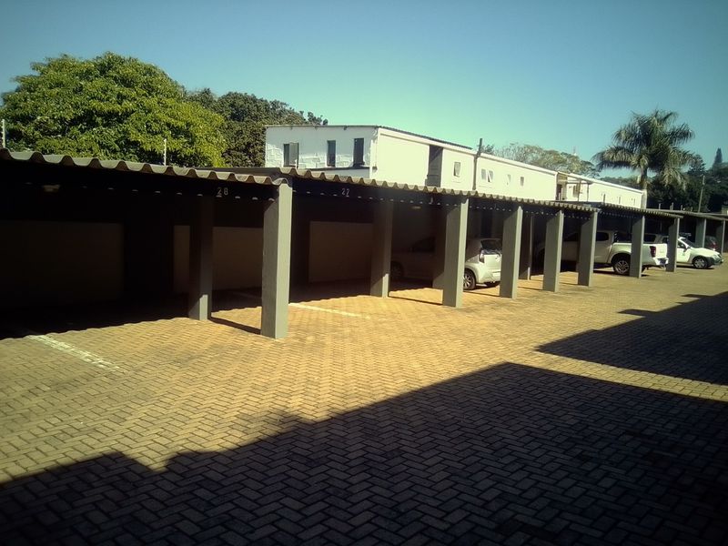 A row of covered parking bays featuring concrete support pillars and a paved driveway area within the apartment complex.
