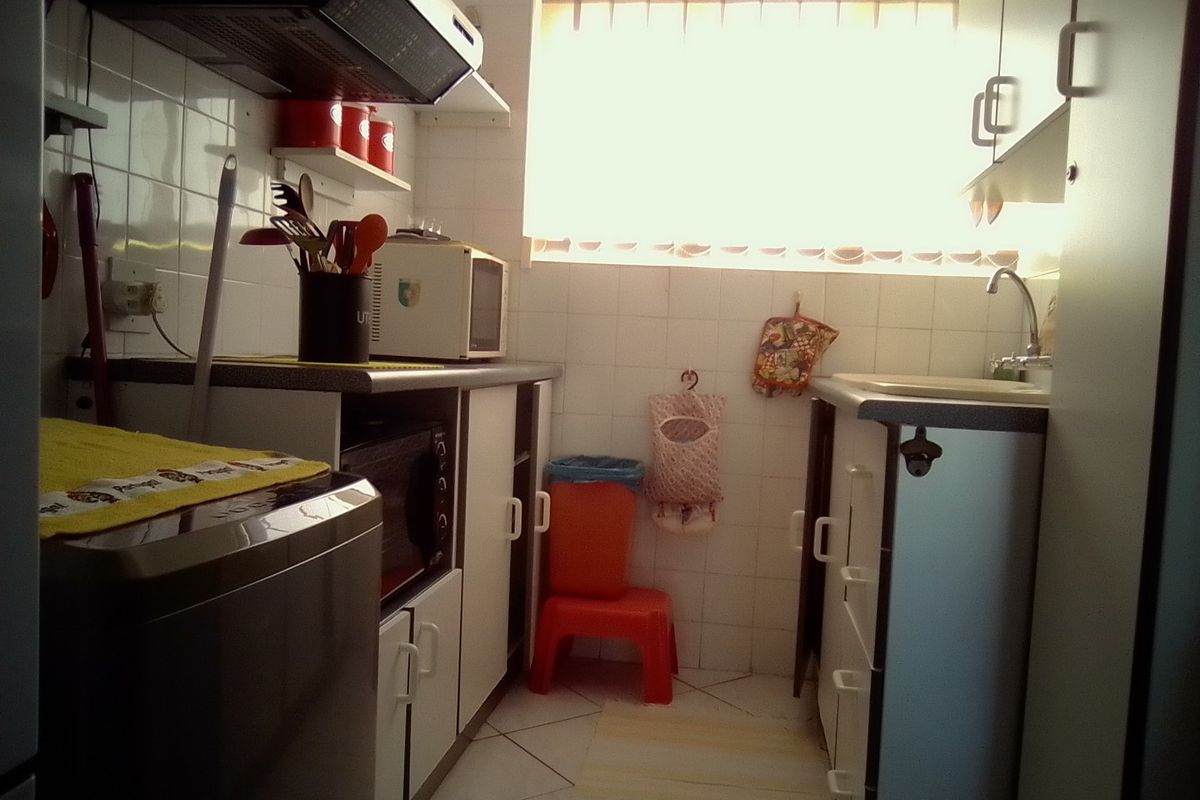 A compact kitchen featuring built-in cabinetry, a tiled backsplash, and a functional sink area with an extractor fan.