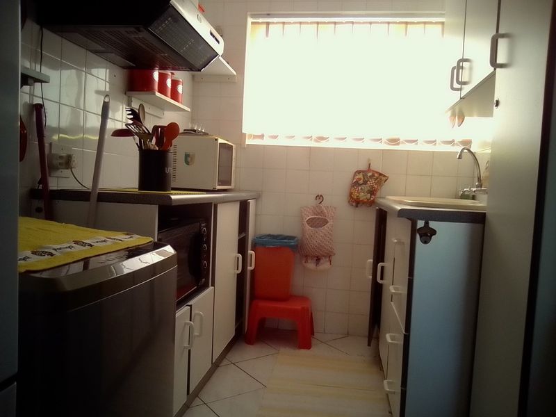 A compact kitchen featuring built-in cabinetry, a tiled backsplash, and a functional sink area with an extractor fan.