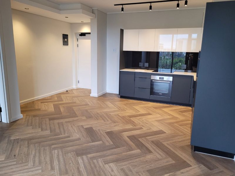 Modern open-plan living area featuring high-quality herringbone timber flooring, sleek built-in kitchen cabinetry with integrated appliances, and contemporary track lighting.