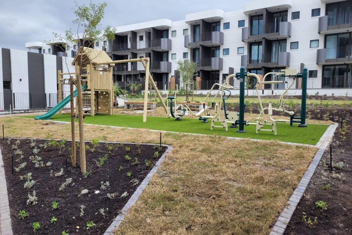 Communal outdoor area featuring a playground and fitness equipment set against a modern apartment building facade.