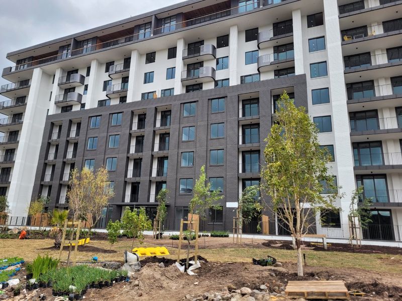 A modern multi-story apartment building featuring a contemporary brick facade, private balconies, and newly landscaped ground-level garden areas.