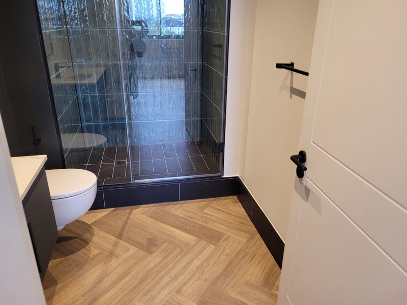 Modern bathroom featuring a walk-in shower with glass enclosure, wall-hung toilet, vanity cabinet, and stylish herringbone flooring.
