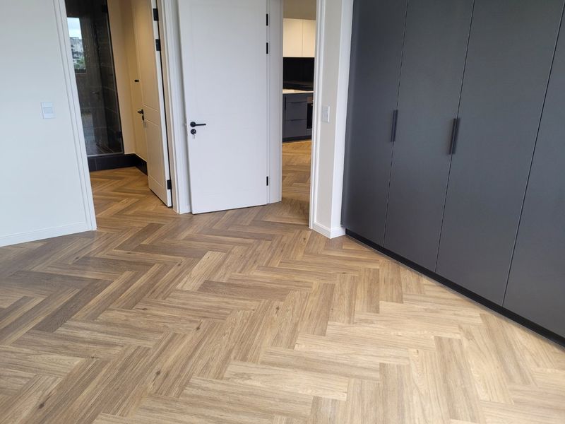 A modern hallway featuring high-quality herringbone timber flooring, sleek dark built-in cabinetry, and clean white interior doors leading to adjacent rooms.