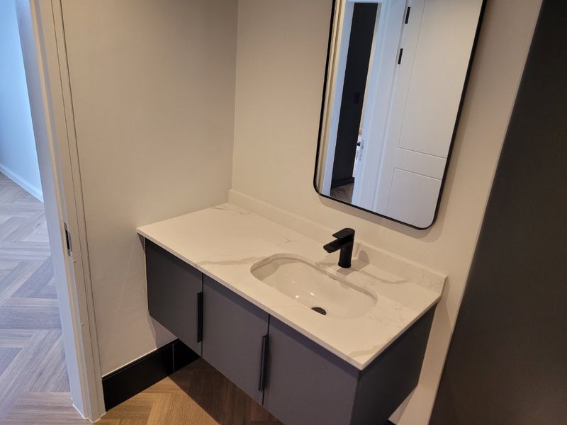 Modern bathroom vanity featuring a stone countertop, undermount sink, matte black faucet, and a sleek wall-mounted mirror set against herringbone flooring.