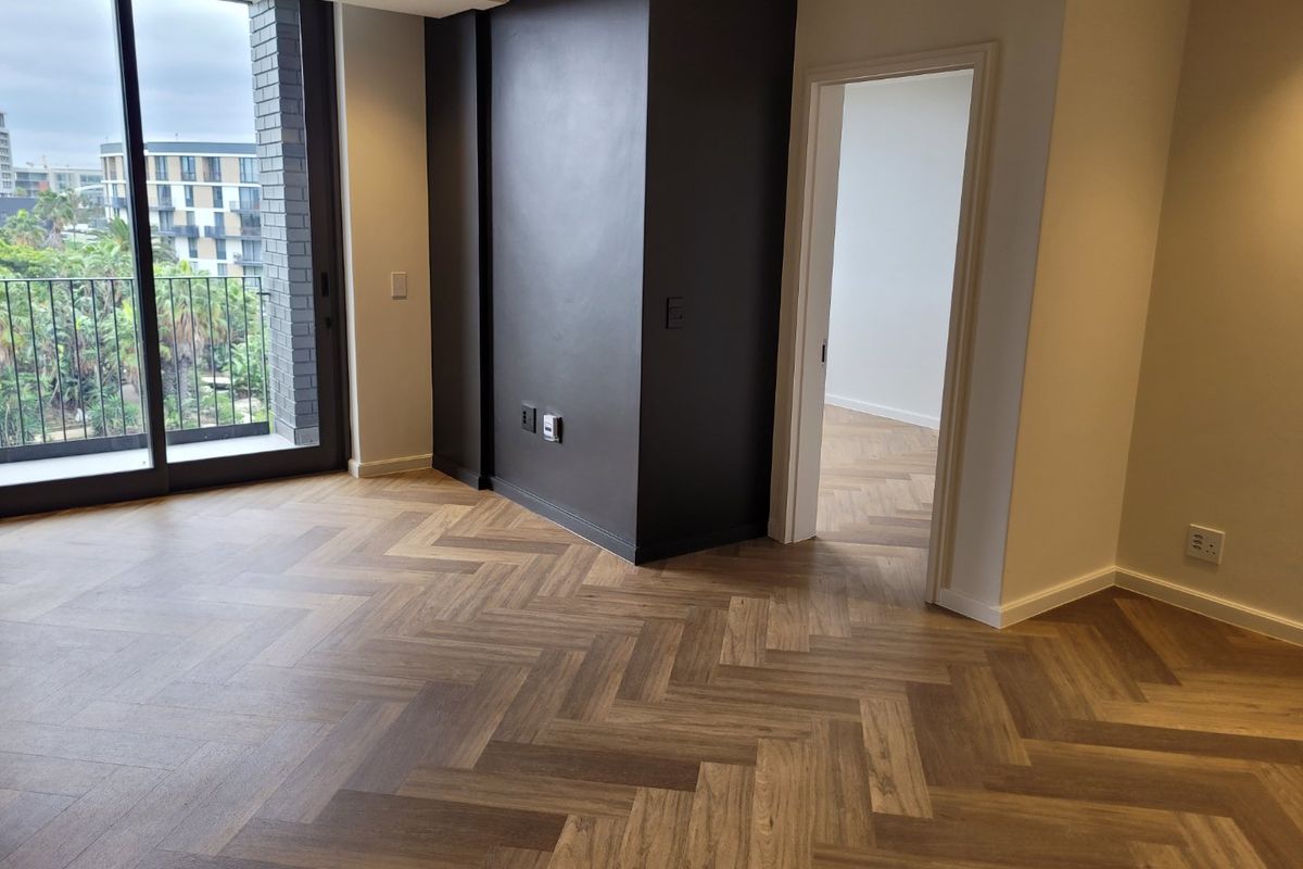 A bright, modern living area featuring elegant herringbone wood flooring, a striking black feature wall, and large sliding doors leading to a balcony.