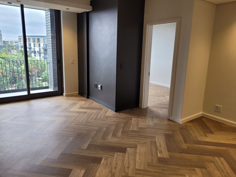 A bright, modern living area featuring elegant herringbone wood flooring, a striking black feature wall, and large sliding doors leading to a balcony.