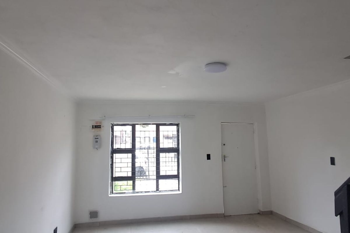An empty living room featuring tiled flooring, a staircase, and security bars on the window. The space is ready for personalization.