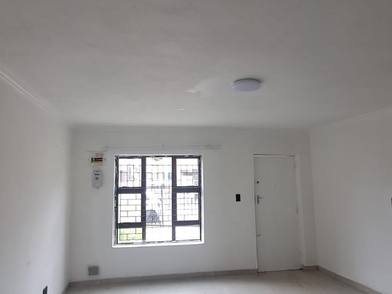 An empty living room featuring tiled flooring, a staircase, and security bars on the window. The space is ready for personalization.