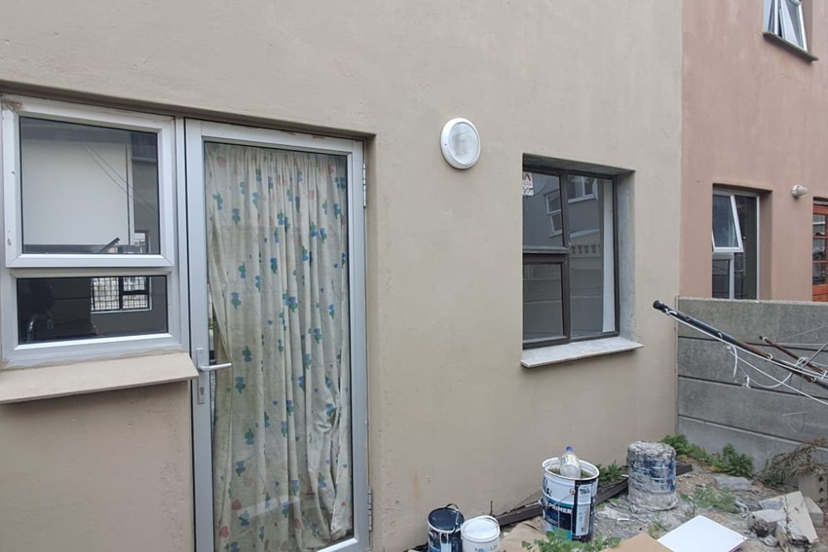 Rear exterior view of the property featuring aluminium window and door frames, with an unfinished garden area requiring landscaping.
